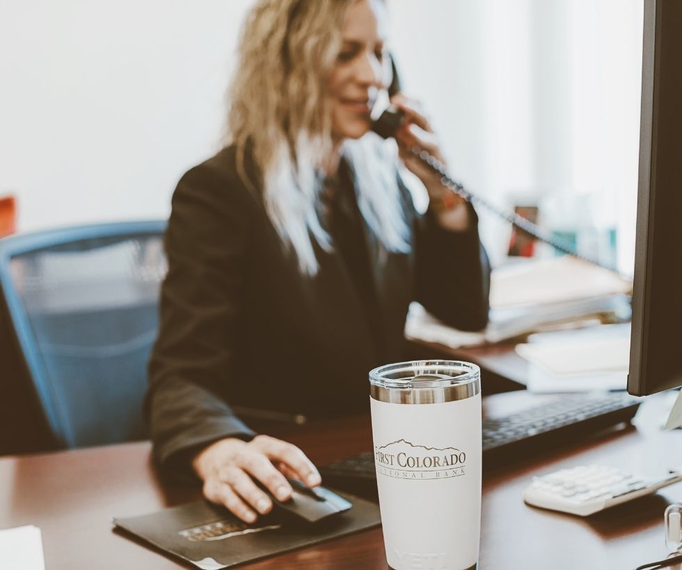 Woman on the phone at a desk with a FCNB cup in focus